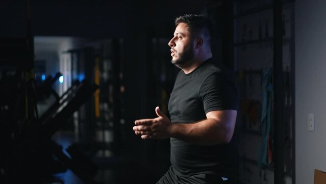 Overweight man alone running in place as a cardio exercise for daily workout in a dark gym training hard dynamic camera movement