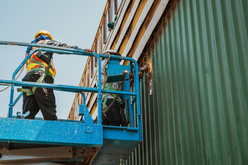 Two workers man on Scissor hydraulic lift or X-lift and use Electric wheel grinding or angle...