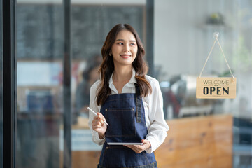 Asian female worker or barista standing smiling and holding the tablet in front of cafe working...