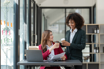 Young Asian and African businesswoman African woman relaxing with coffee mug while brainstorming investment plan Financial business together in the office management concept.