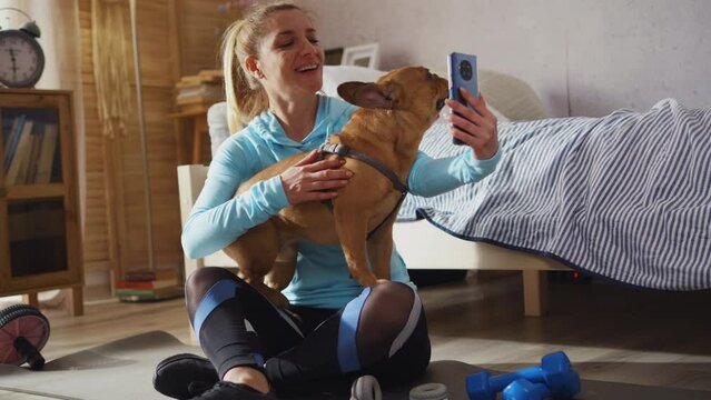 Sporty adult fit woman making selfie shot with a pet dog in bedroom