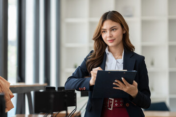 Confident young asian businesswoman standing writing with pen recording plans, financial goals,...