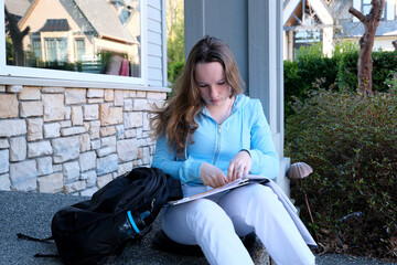 teenager girl does homework on porch of house she writes with pencil in large notebook notebook in...