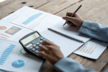 Image of hands of businesswoman, investor, pressing calculator to calculate numbers Income and record data in a notebook from the graph. Chart showing financial results in real estate projects.