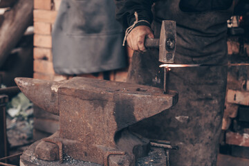 Blacksmith process glowing metal with hammer on anvil in forge. Dirty hands of farrier strike iron...