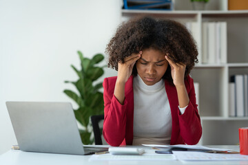 Young American businesswoman working on the laptop with documents and stressing at work from...