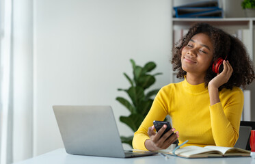 Startup businesswoman, American woman African woman wearing headphones music and holding mobile phone using bluetooth listening music while sitting resting after work happily and relaxing at office.