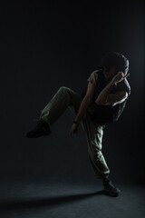 Silhouette of a male dancer dancing in the dark. Handsome fashionable man with sunglasses wearing fashionable clothes with cap, vest and sneakers dancing in motion on a black background