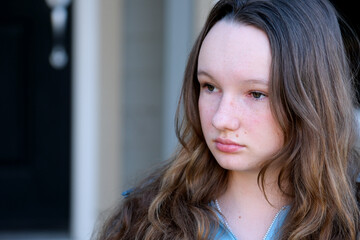 beautiful face of a young teenager girl close-up girl leaned over draws or writes looks down against the background of a building of green leaves lessons thinking dreaming expectation sadness