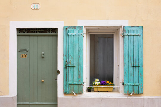 Vieille maison typique aux volets verts au num&eacute;ro 10 d'une ruelle d'un village du sud de la France avec fleurs en rebord de fen&ecirc;tre et porte en bois avec heurtoir.