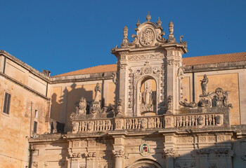 Fachada norte de la catedral de la Asunción de Santa María en Lecce, Italia. Detalles arquitectónicos barrocos del entablamento sobre el portal con la estatua de San Oroncio en el centro.