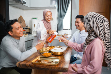 muslim woman serving drink for her friend and family at home having dinner together