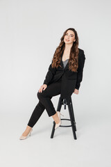young businesswoman with long curly hair in a black suit sitting on a white background