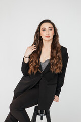 young businesswoman with long curly hair in a black suit sitting on a white background