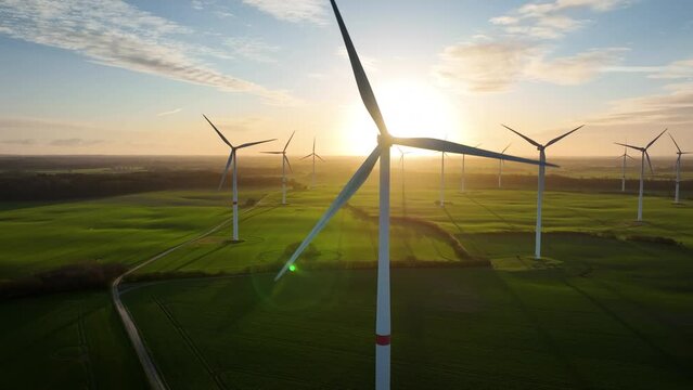 Aerial footage of wind farm by sunrise with wind turbine, which rotors by spin momentarily concealing the sun and causing a fascinating play of light and shade. Large spinning wind turbine.