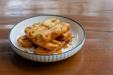Delicious snack fried bananas or pisang goreng served with honey syrup on white bowl