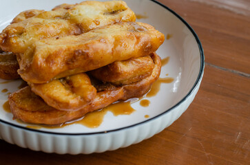 Close up of delicious snack fried bananas or pisang goreng served with honey syrup on white bowl