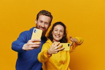 Man and woman couple smiling merrily with phone in hand social media viewing photos and videos, on yellow background, symbols signs and hand gestures, family freelancers.