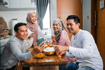 happy friends taking their picture together using a smartphone while having iftar dinner