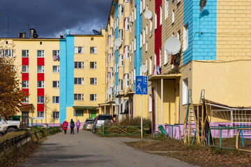 Fototapeta na wymiar View of the street and colorful buildings in a small town. Children with school bags go home. Autumn season. Everyday life in provincial towns and villages in Russia. Klyopka, Magadan Region, Russia.