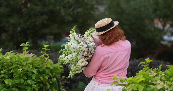 woman in pink shirt holding a bouquet of white flowers on the background of green garden, summer, spring concept. 4k footage