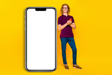 Full size photo of cheerful satisfied person stand near huge phone isolated on yellow color background