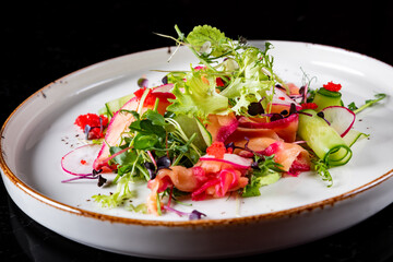 Green salad with salmon, cucumbers, lettuce, spices, caviar in plate