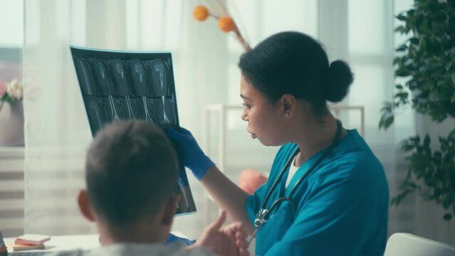 Female surgeon checking bone fracture on x-ray scan, talking to boy patient