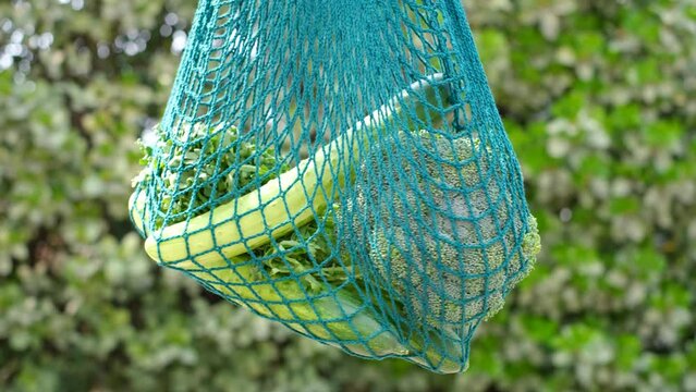 Reusable shopping bags with vegetables on green background, zero waste concept.
