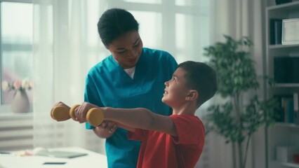 Little boy doing dumbbell exercise with help of doctor at rehabilitation center - Powered by Adobe