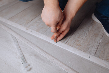 The builder's hand holds a screwdriver in his hands and is engaged in covering the floor. Lay laminate flooring in the apartment.