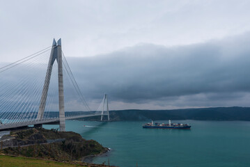 The 3rd bridge, located at the Black Sea exit of the Bosphorus, and the ship passes through the blue waters under it in cloudy weather.