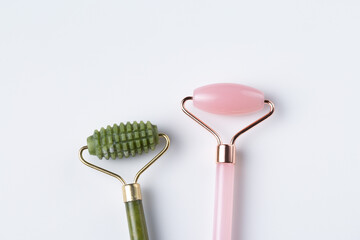 Two cosmetic facial rollers, rose quartz crystal and jade isolated on white background, top view