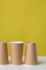 Disposable cardboard biodegradable glass on a white table, yellow background.