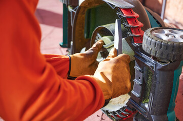 Hands of an unrecognizable gardener holding a file to sharpen mower blades. Backyard lawn...