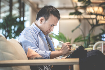 Asian man using a tablet drawing a graphics on tablet in a modern coffee shop, Technology in use concepts