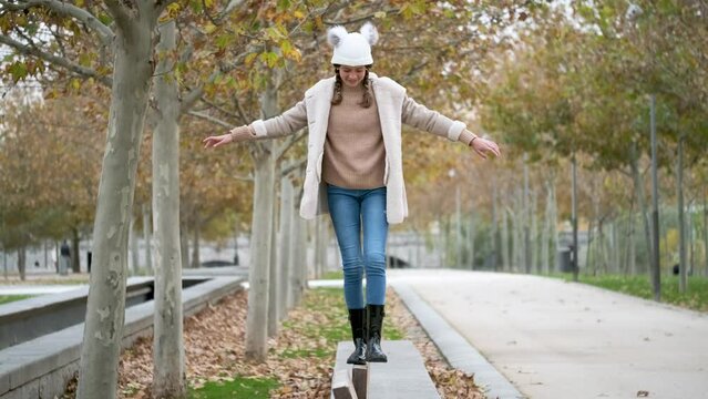 Preteen girl with two braids walking on balance beam outdoors in autumn.