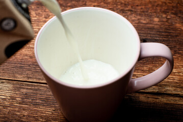 Milk is poured into a cup on a brown wooden background.