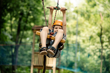 A young boy is hanging on the line in the rope park. Sports entertainment for a child, active rest. © Konstiantyn Zap