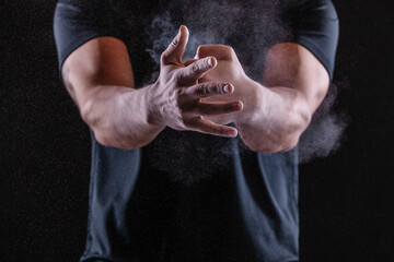 Fototapeta na wymiar Young strong sportsman applying chalk powder on hands against black background. Man punching his palm hand.