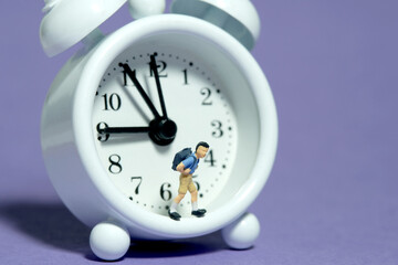 Miniature tiny people toy photography. A boy student with backpack standing on clock. Isolated on...
