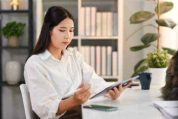 Fototapeta premium Modern millennial woman using digital tablet, working from home in cozy interior