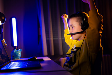 Young excited boy gamer with headphone playing video game on laptop at home.