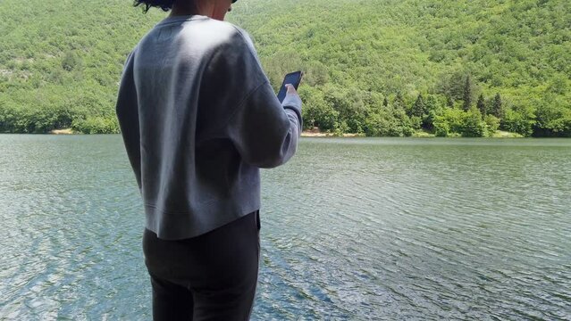 Hiker woman using her phone to check the location and the map while hiking on a mountain near a lake