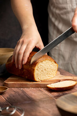 Woman cutting sourdough white loaf bread on wooden board. Homemade healthy cooking concept.