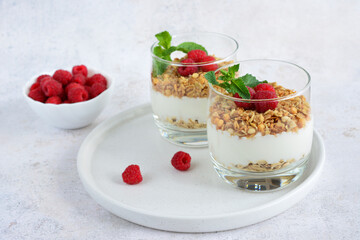 Two glasses of granola with raspberries and mint leaves on a white tray isolated, close-up
