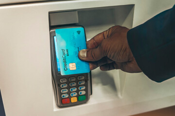 Man paying with NFC technology on credit card, restaurant, shop. Contactless Payment System. Afro guy in suit holding credit card close to electronic payment machine, paying for delivery