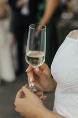 Woman in white dress holding champagne coupe in hands. The concept of a party.
