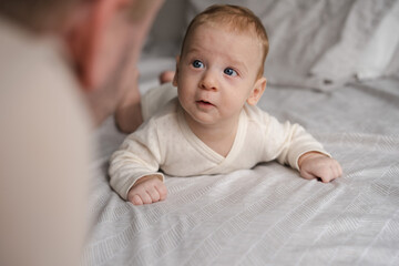 Cute two or three months baby boy looking at his parent or adult lying on belly on bed.Copy space.