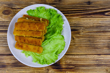 Baked fish sticks and lettuce leaves in a plate. Top view